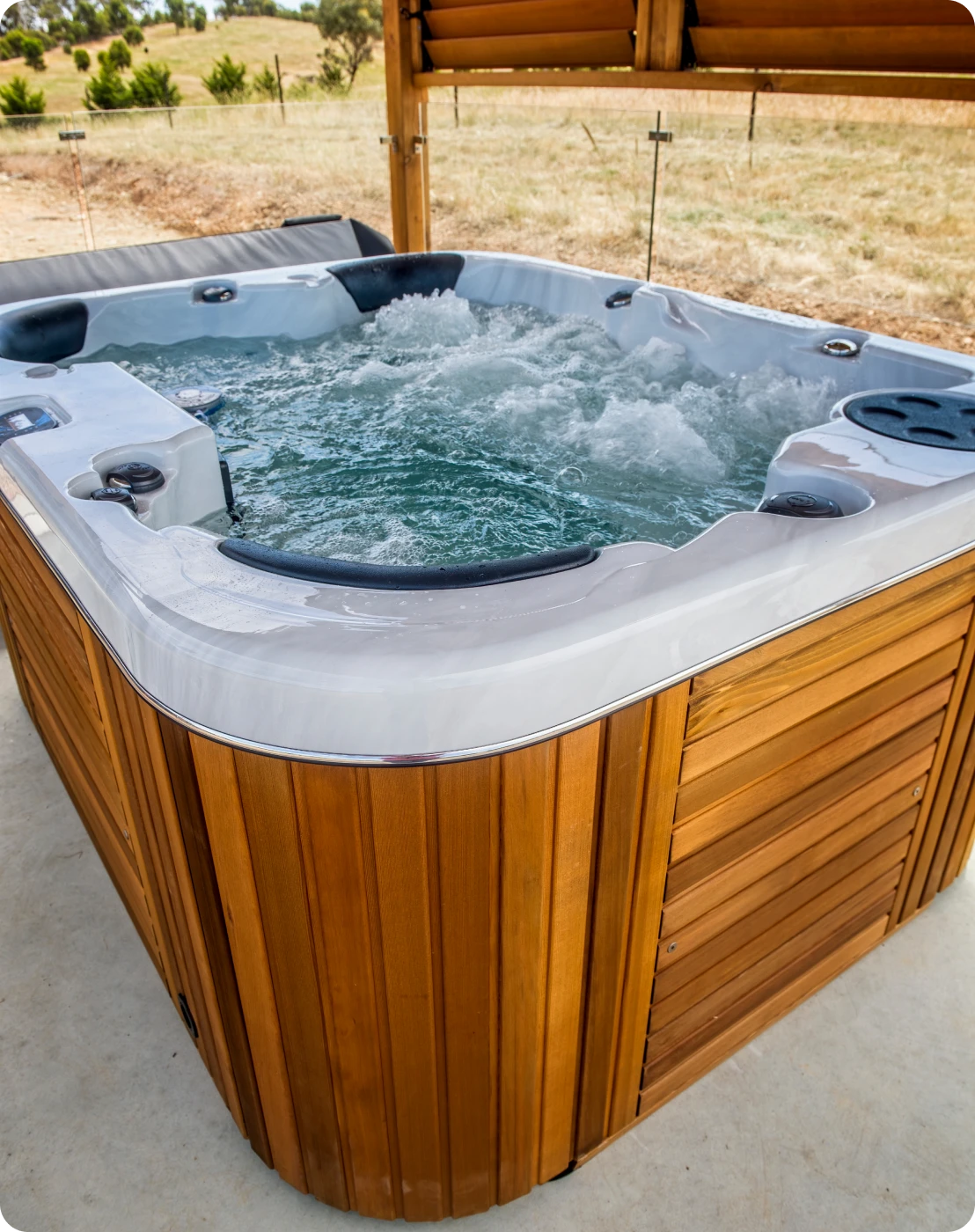 A modern wooden hot tub filled with bubbling water outdoors.