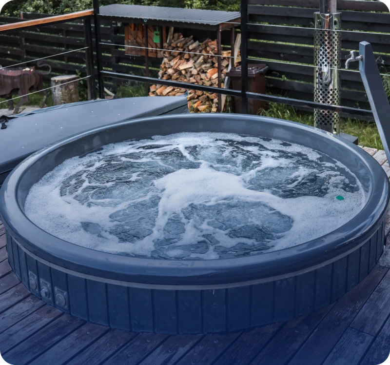 A bubbling blue hot tub on a wooden deck outdoors.
