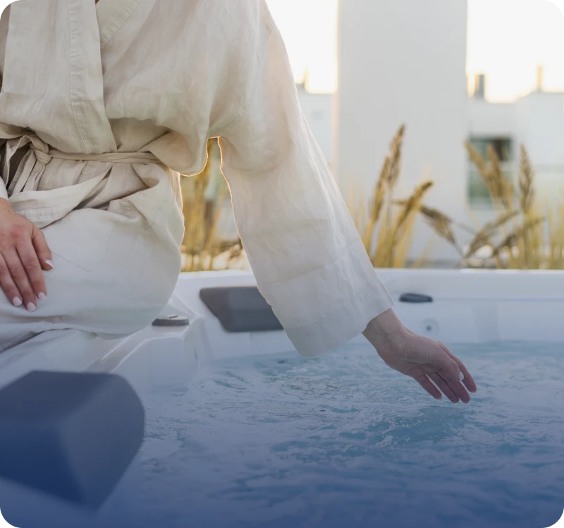 Person touching calm water in a white outfit near a pool.