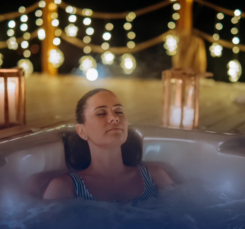 Woman relaxing in a hot tub under warm string lights.